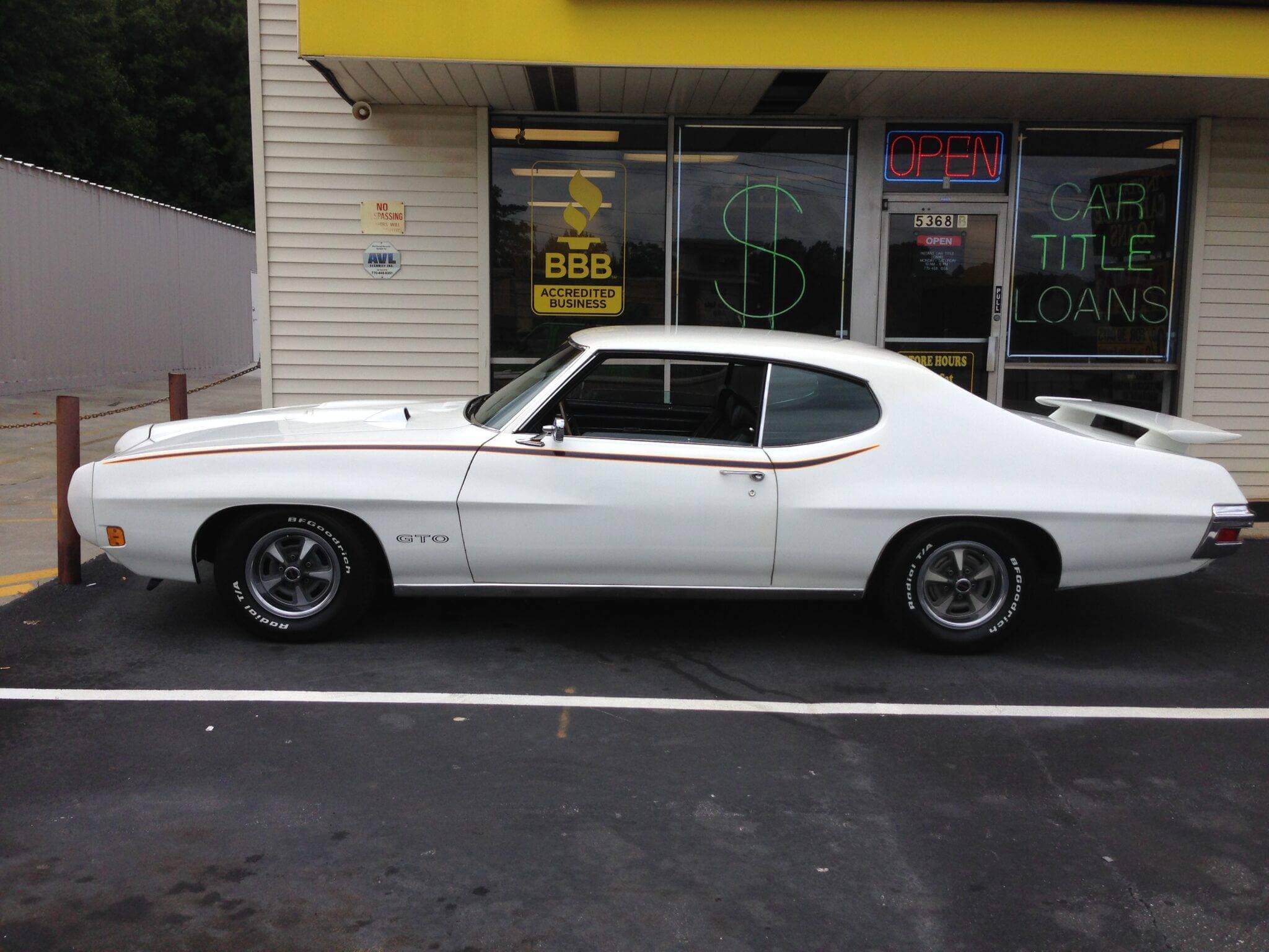 Classic white muscle car parked outside a shop.