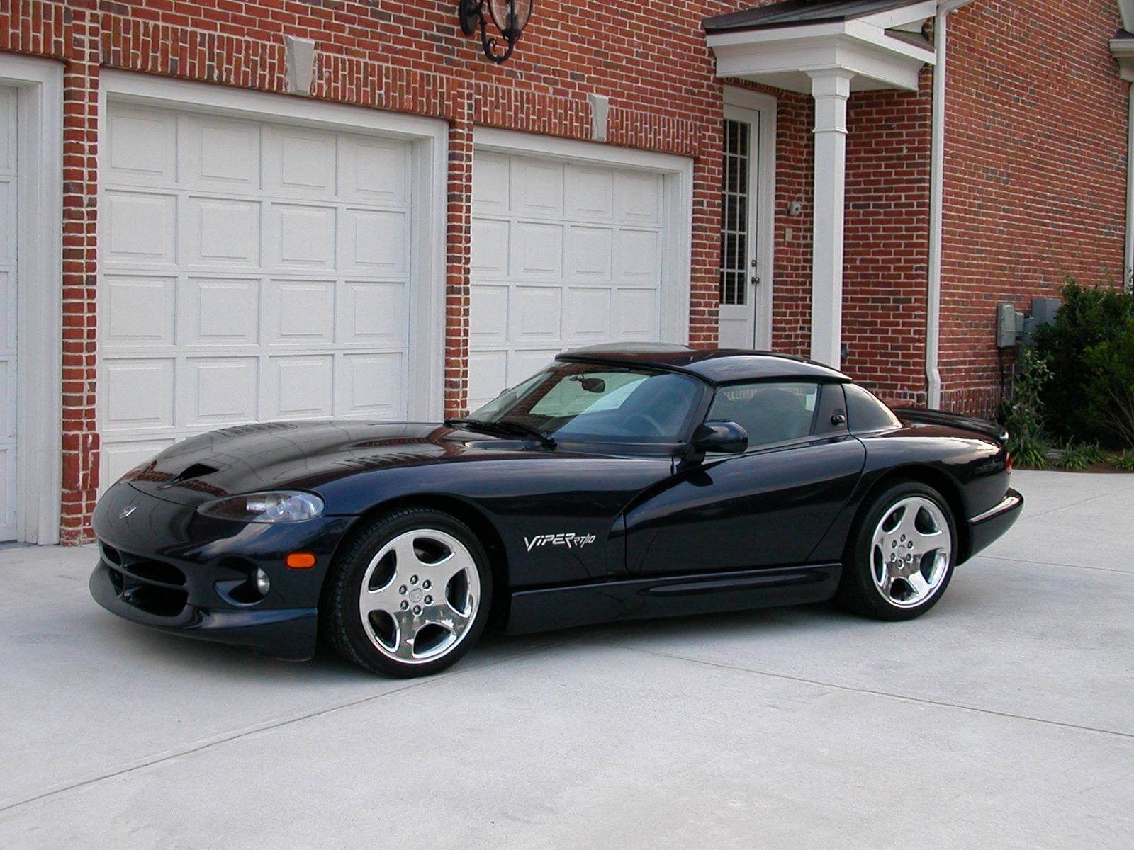 Black Dodge Viper parked in front of a brick house garage.