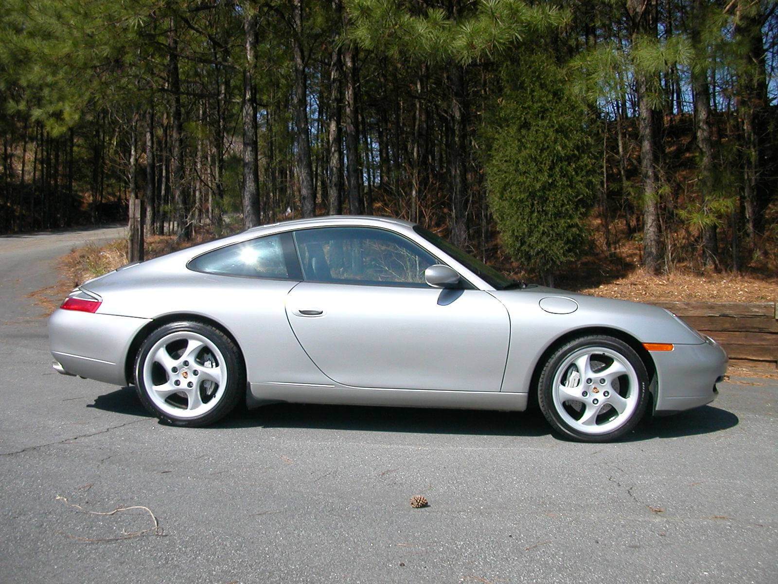 Silver sports car parked on a road near trees.