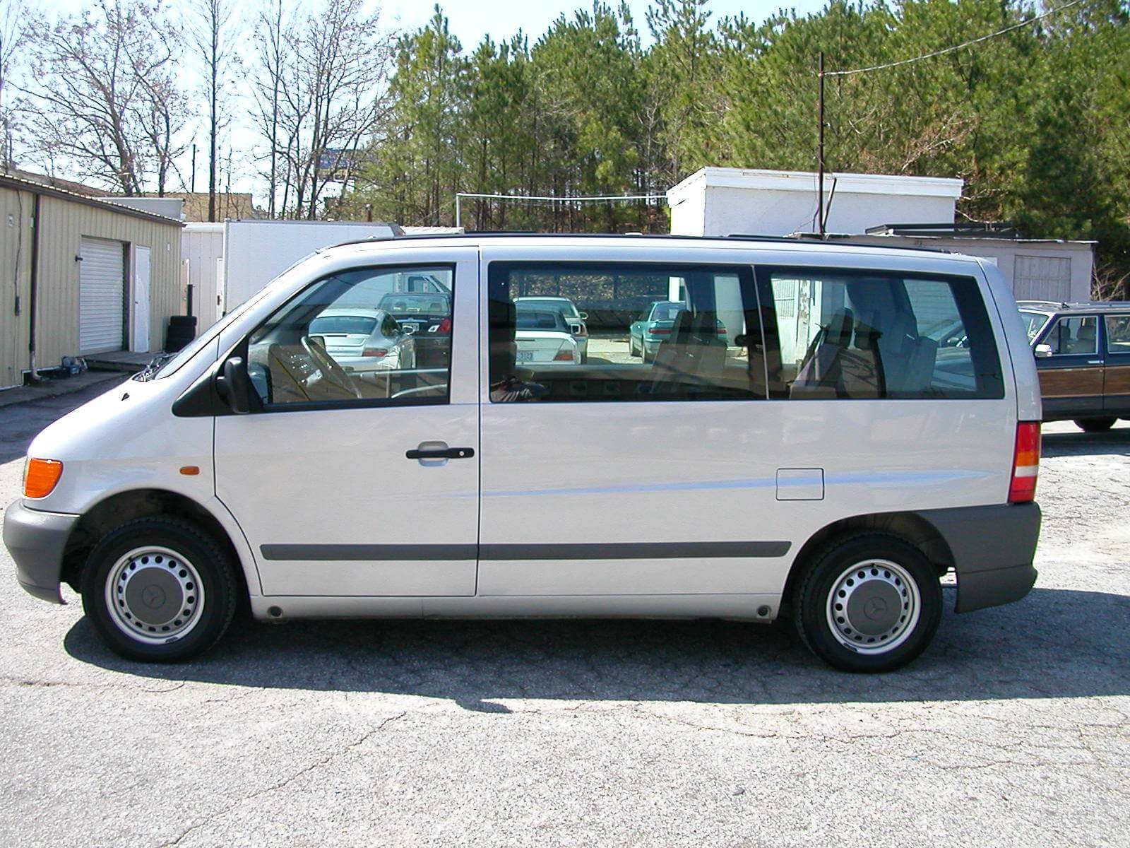 White van parked on a sunny day near trees and trailers.