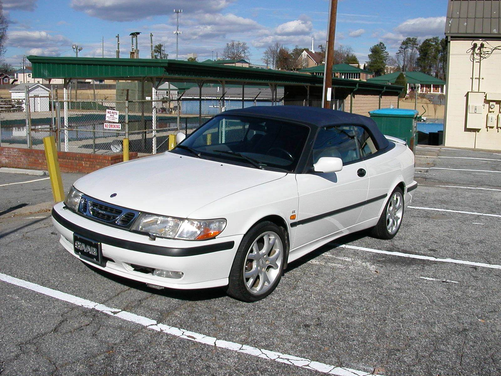 White convertible car parked in an outdoor lot under a partly cloudy sky.