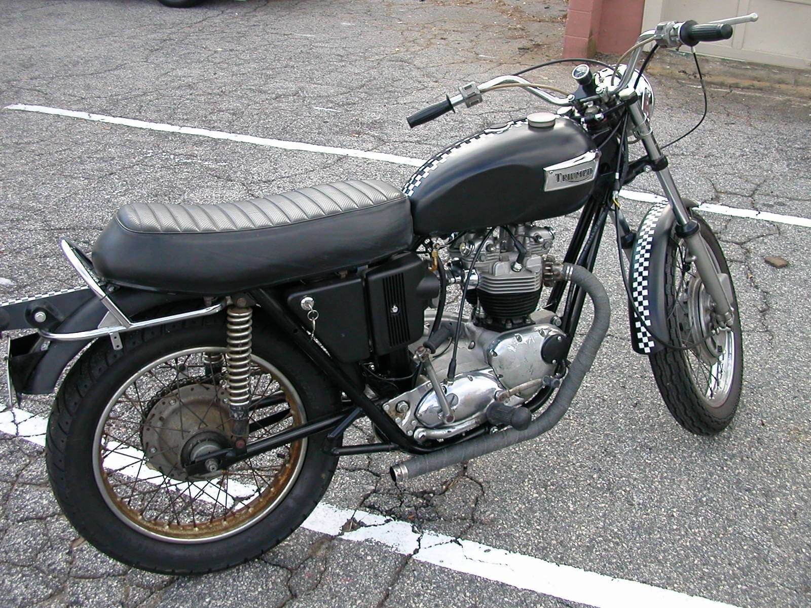 Vintage black motorcycle parked on a street with a quilted seat.
