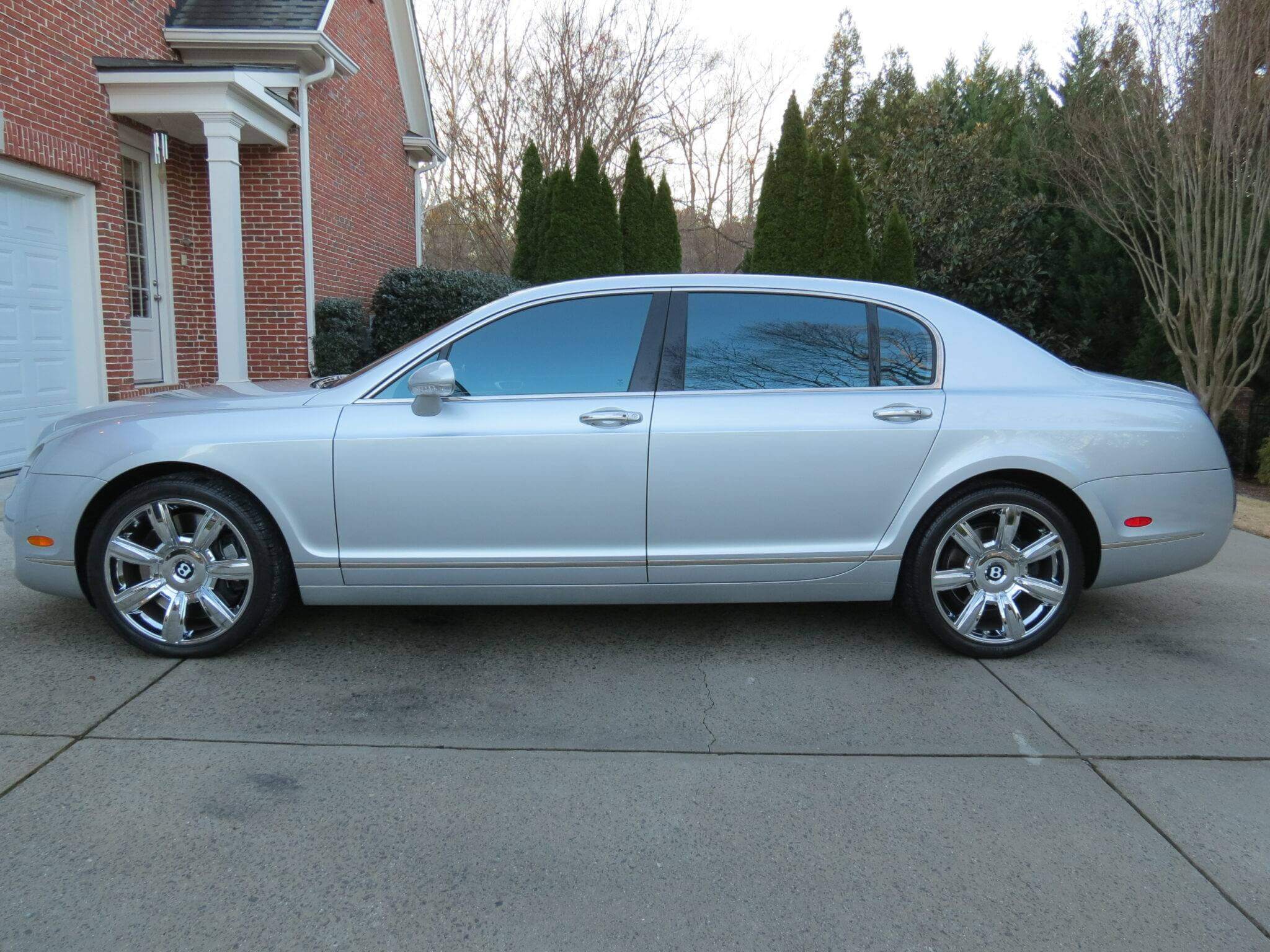 Silver luxury sedan parked in driveway beside a brick house.