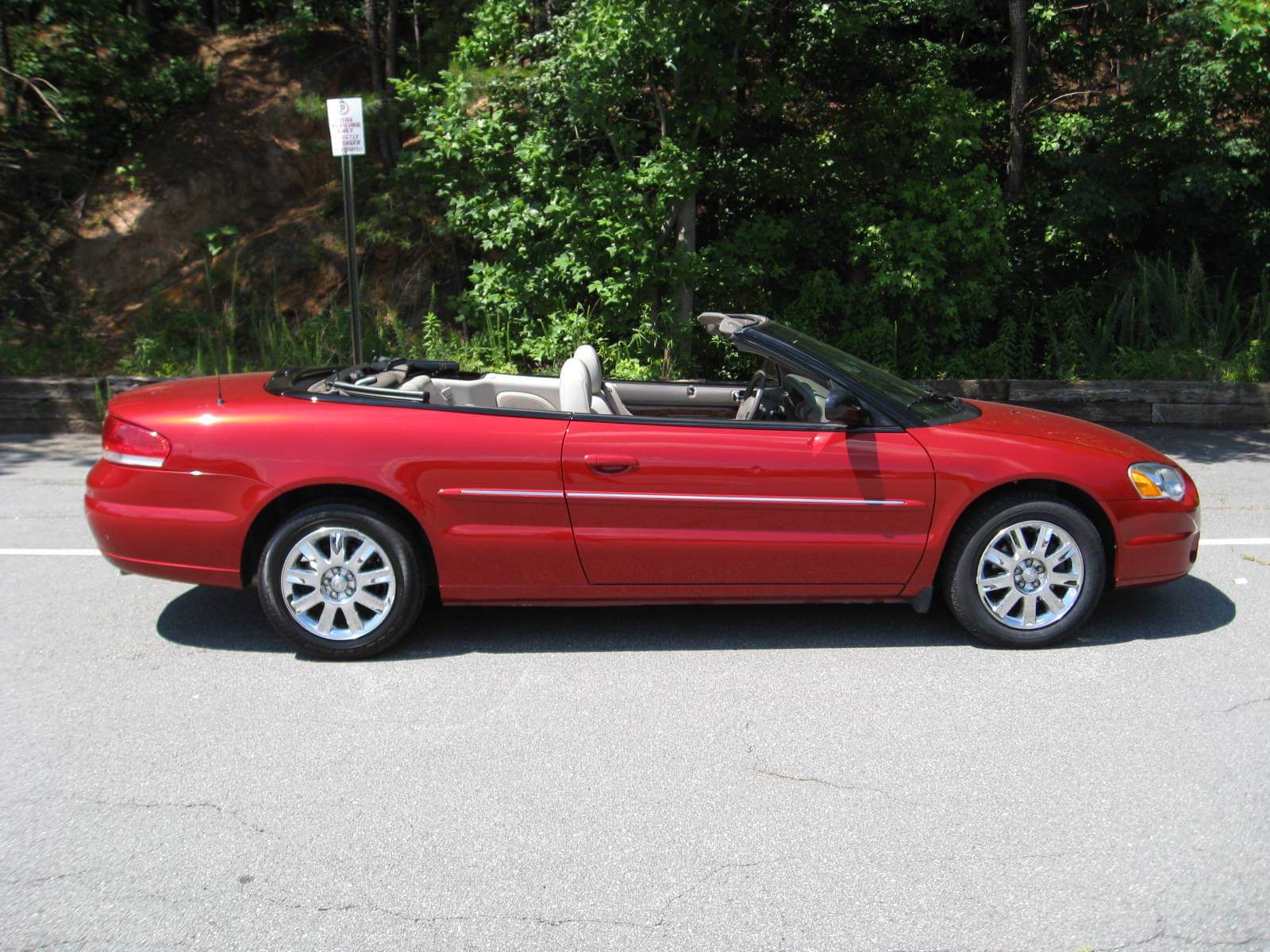 Red convertible car parked on a street with trees in the background.