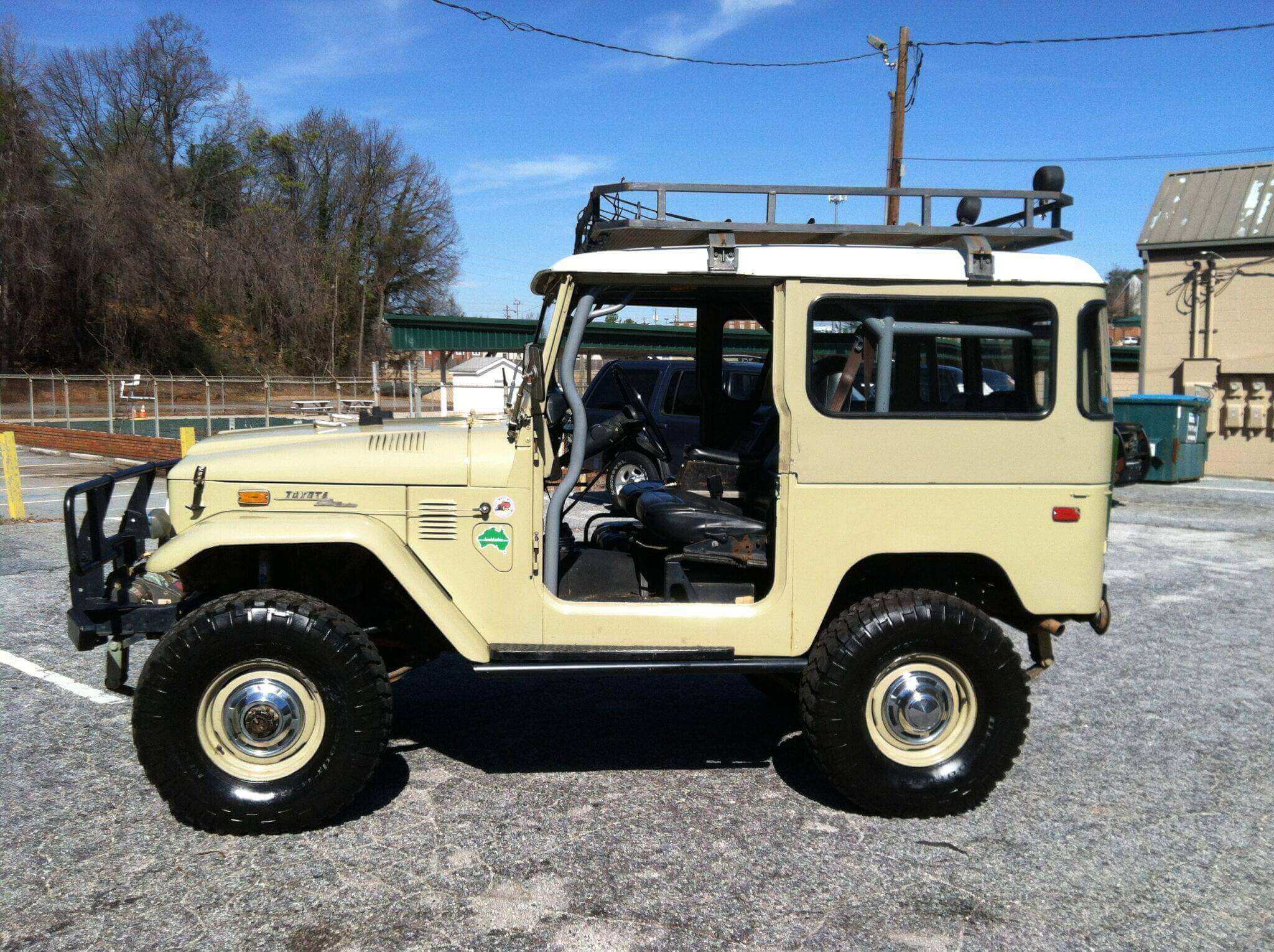 Vintage beige off-road vehicle with open doors parked on gravel.