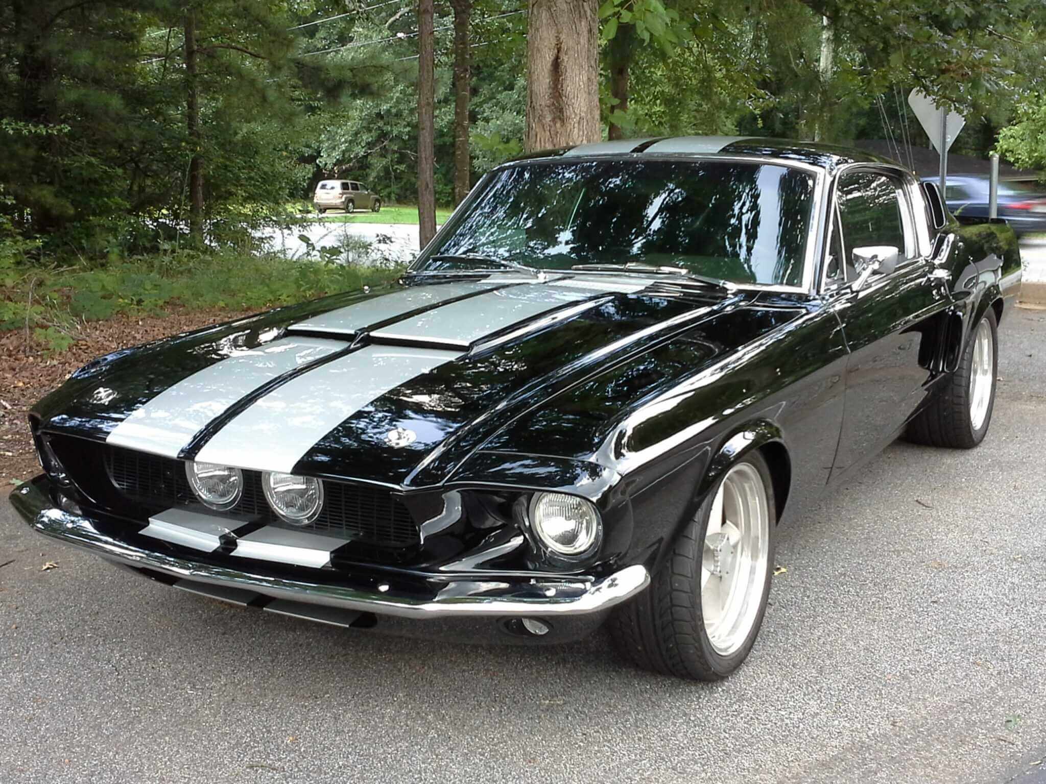 Classic black muscle car with white racing stripes parked outdoors.