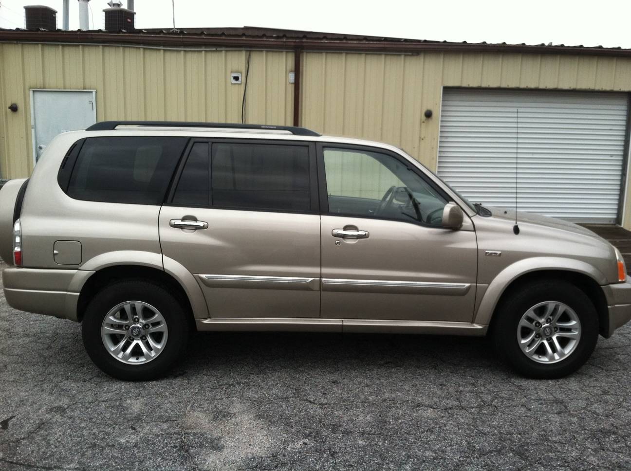 Beige SUV parked on gravel near a metal building with garage doors.