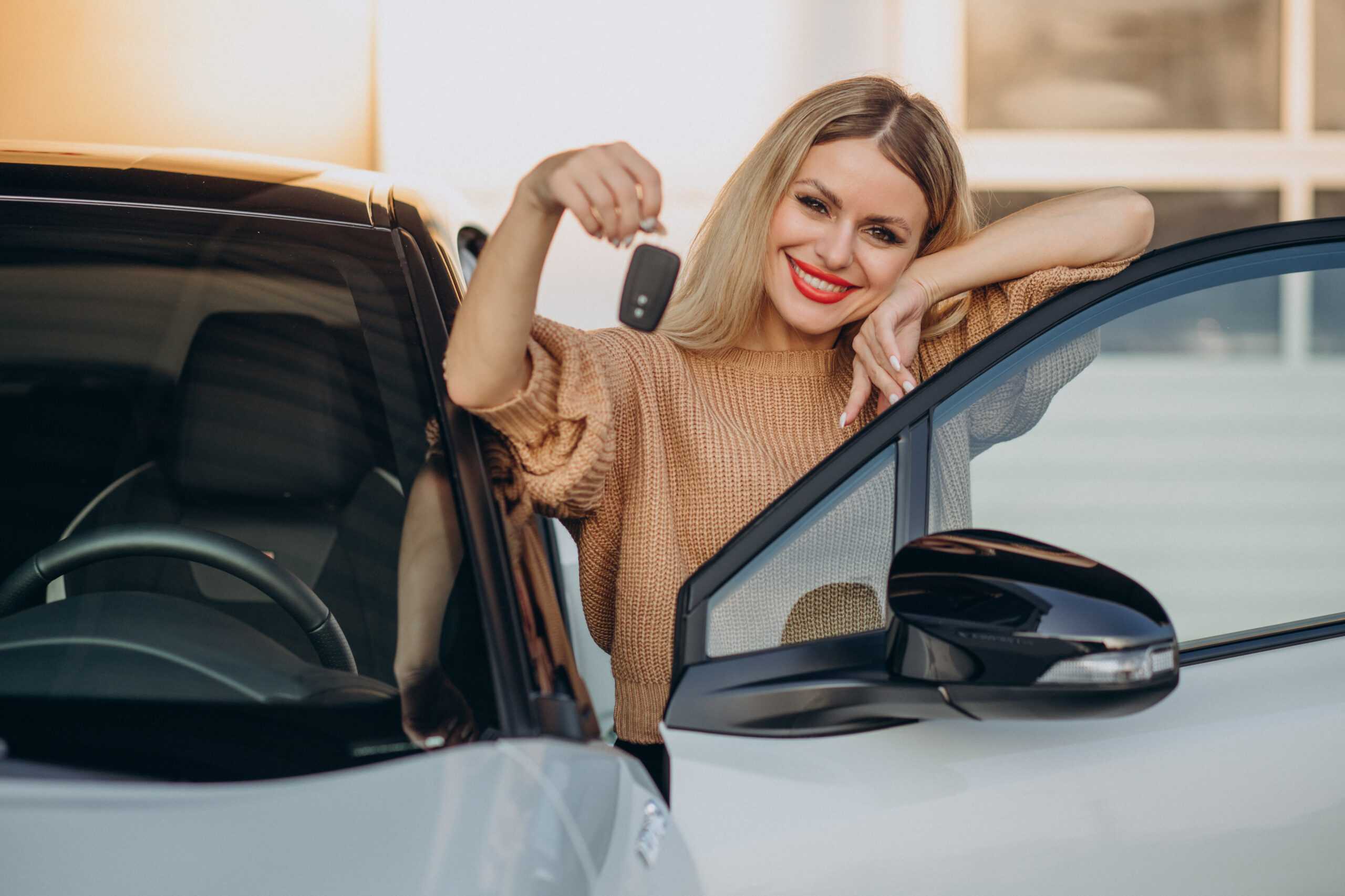 Woman happily holding car keys next to a black car.